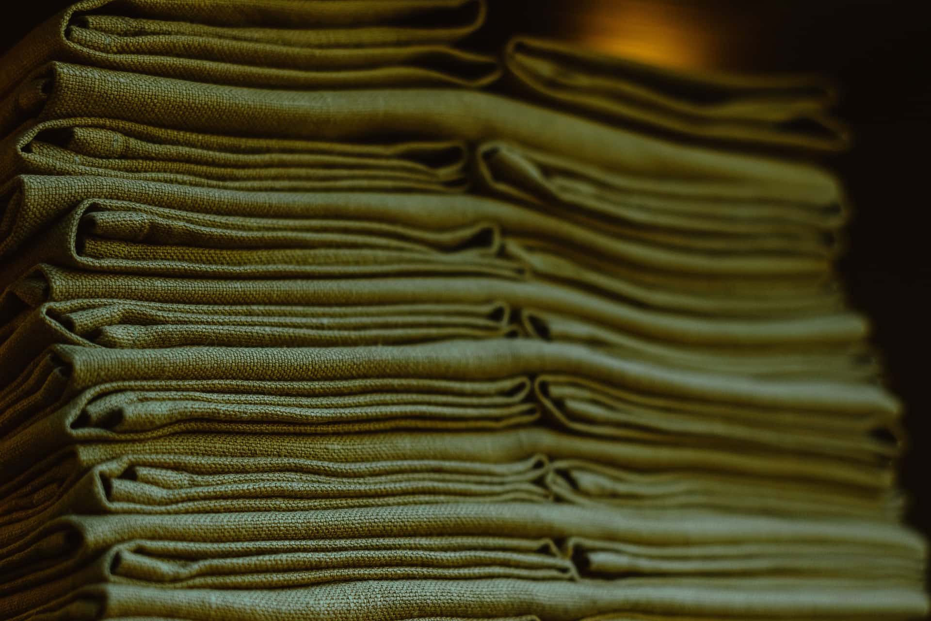 Folded technical fabrics stacked on a workbench in low directional light
